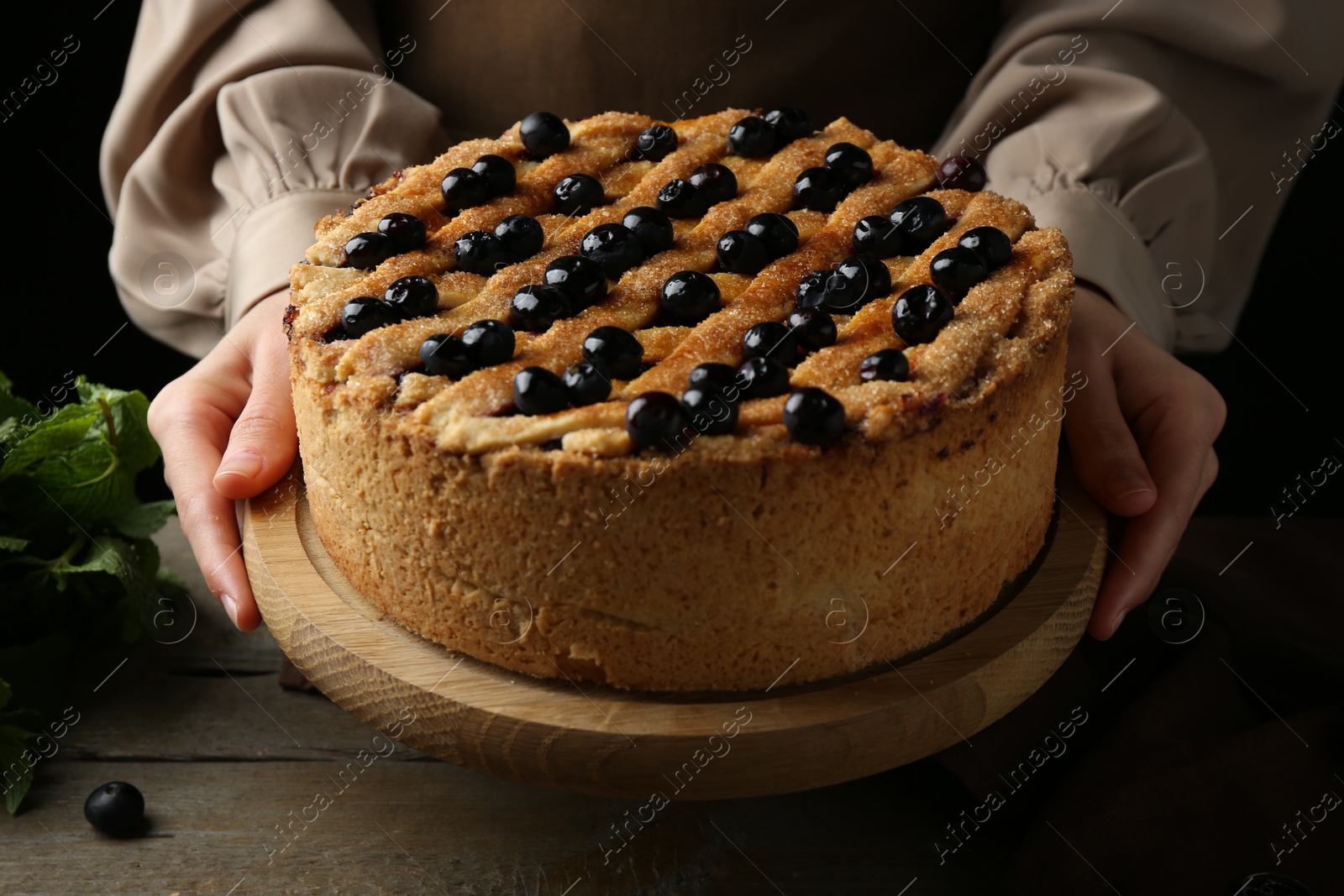 Photo of Woman with homemade blueberry pie at wooden table, closeup