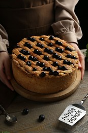 Photo of Woman with homemade blueberry pie at wooden table, closeup