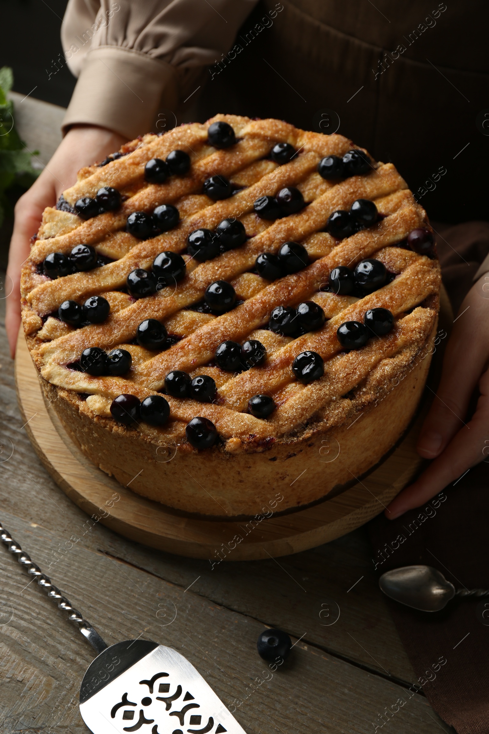 Photo of Woman with homemade blueberry pie at wooden table, closeup