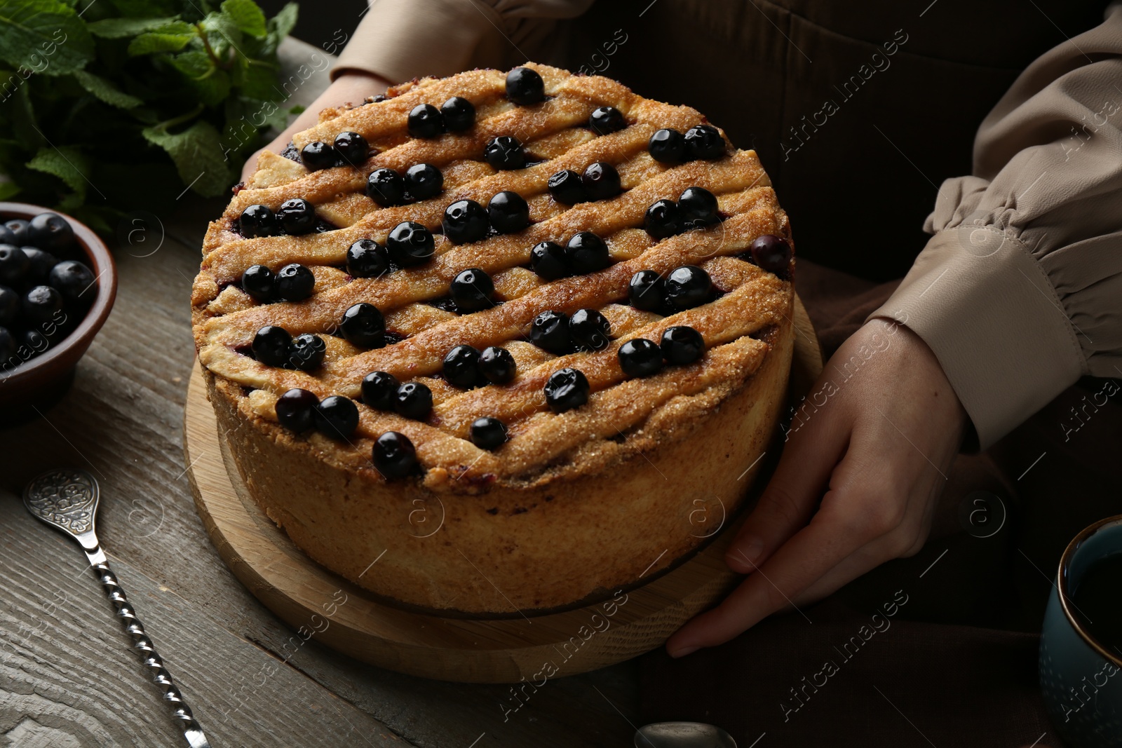 Photo of Woman with homemade blueberry pie at wooden table, closeup