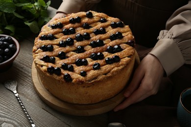 Photo of Woman with homemade blueberry pie at wooden table, closeup