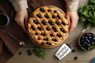 Photo of Woman with homemade blueberry pie at wooden table, top view