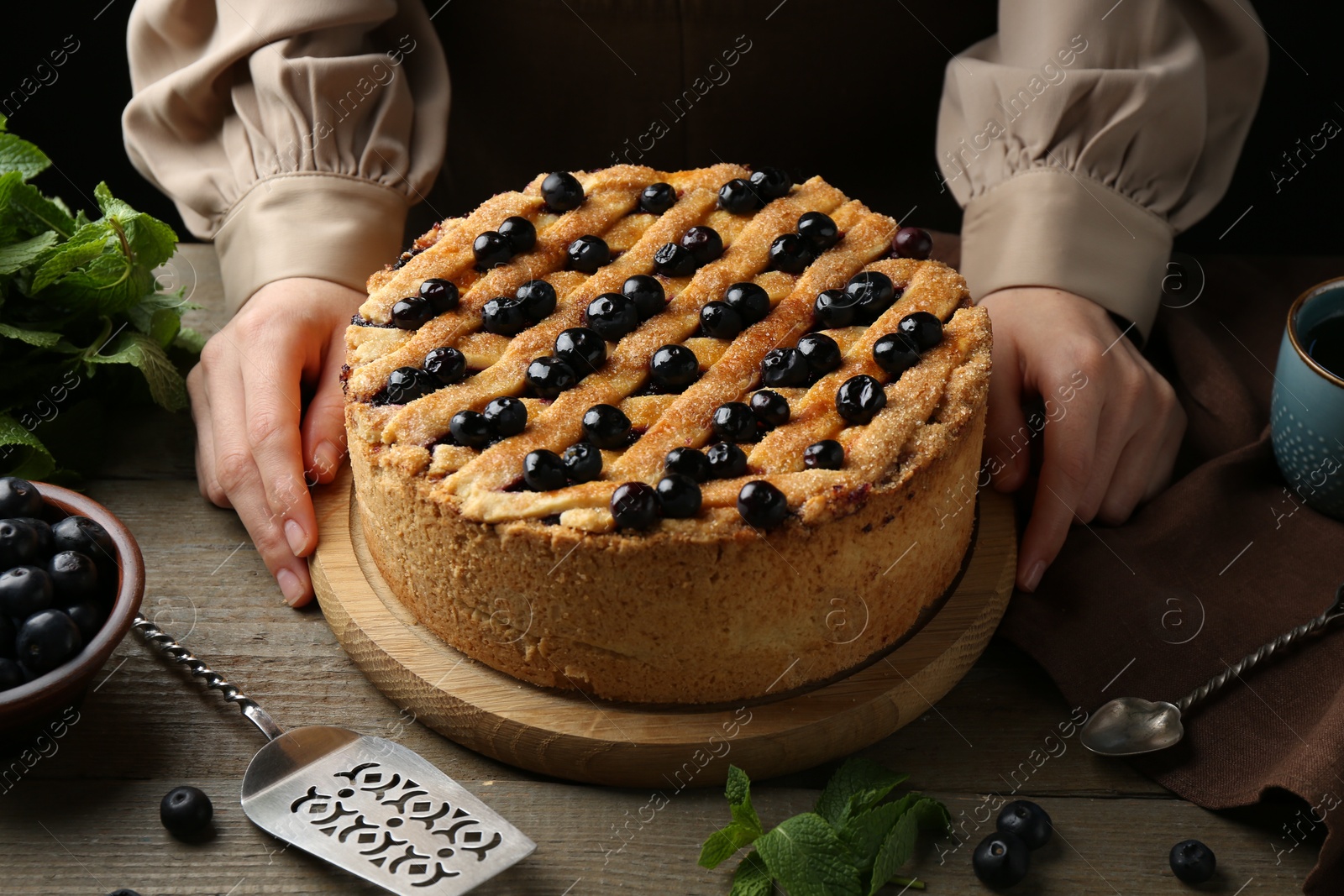 Photo of Woman with homemade blueberry pie at wooden table, closeup