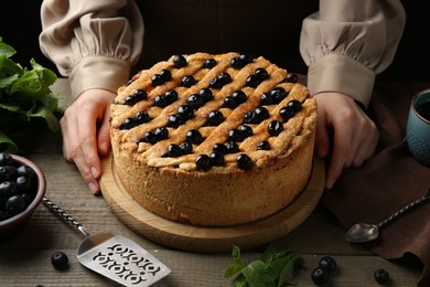 Photo of Woman with homemade blueberry pie at wooden table, closeup