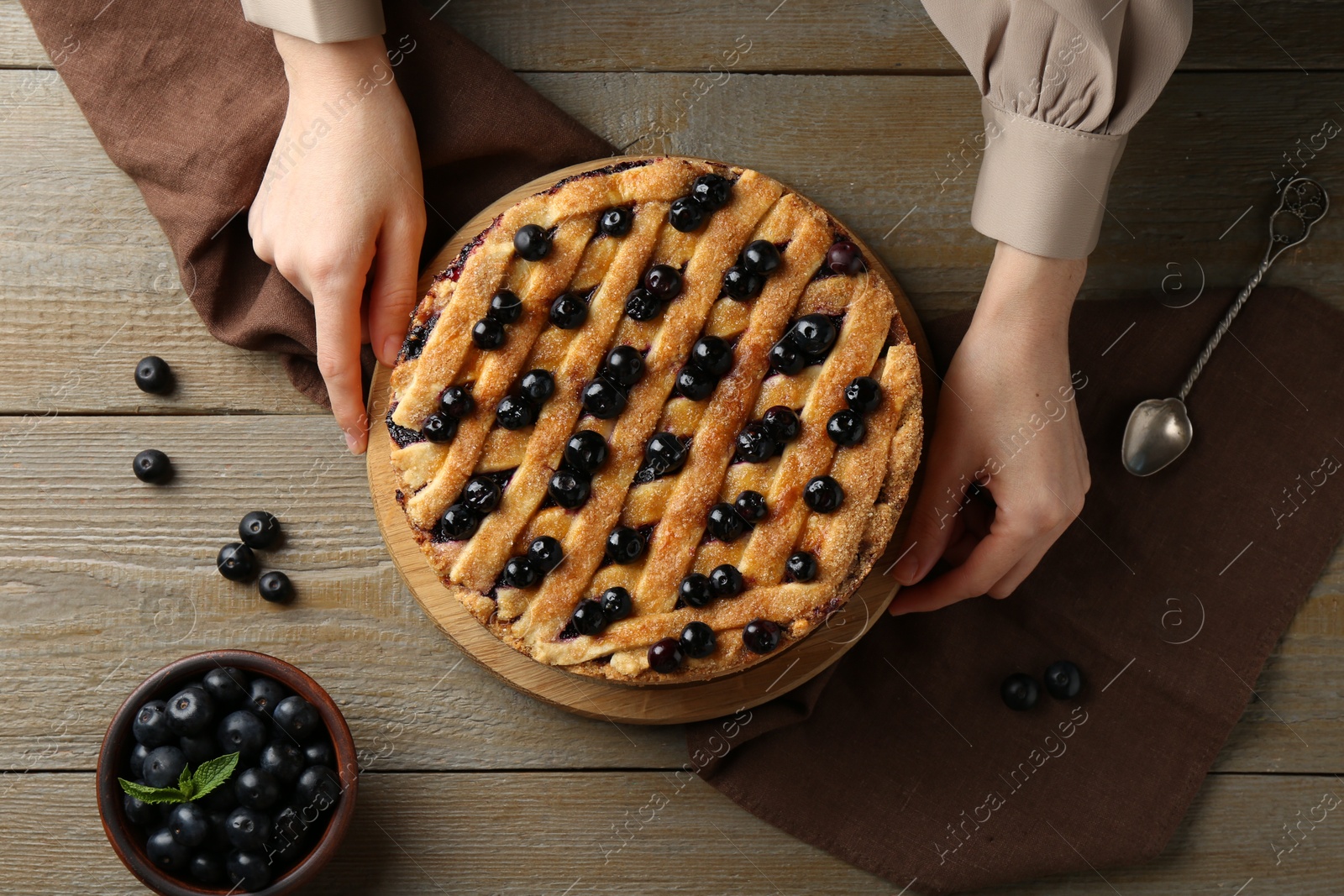 Photo of Woman with homemade blueberry pie at wooden table, top view