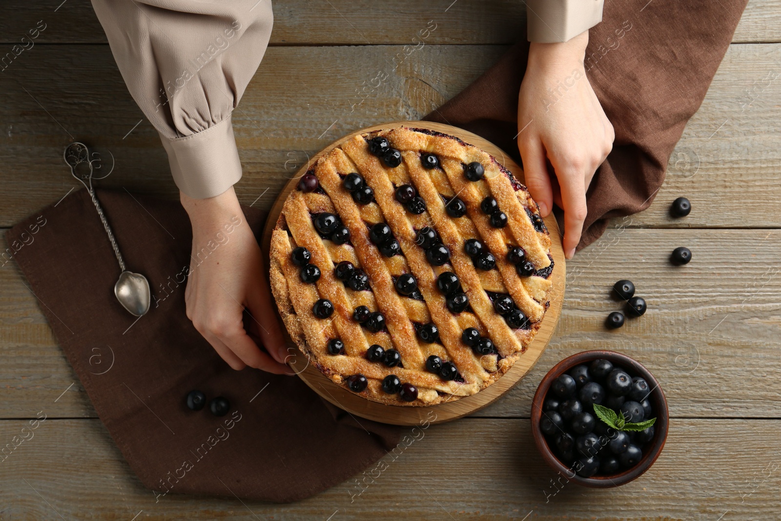 Photo of Woman with homemade blueberry pie at wooden table, top view