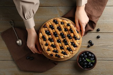 Photo of Woman with homemade blueberry pie at wooden table, top view