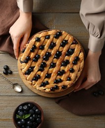 Photo of Woman with homemade blueberry pie at wooden table, top view