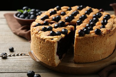 Photo of Taking slice of homemade blueberry pie and fresh berries on wooden table, closeup