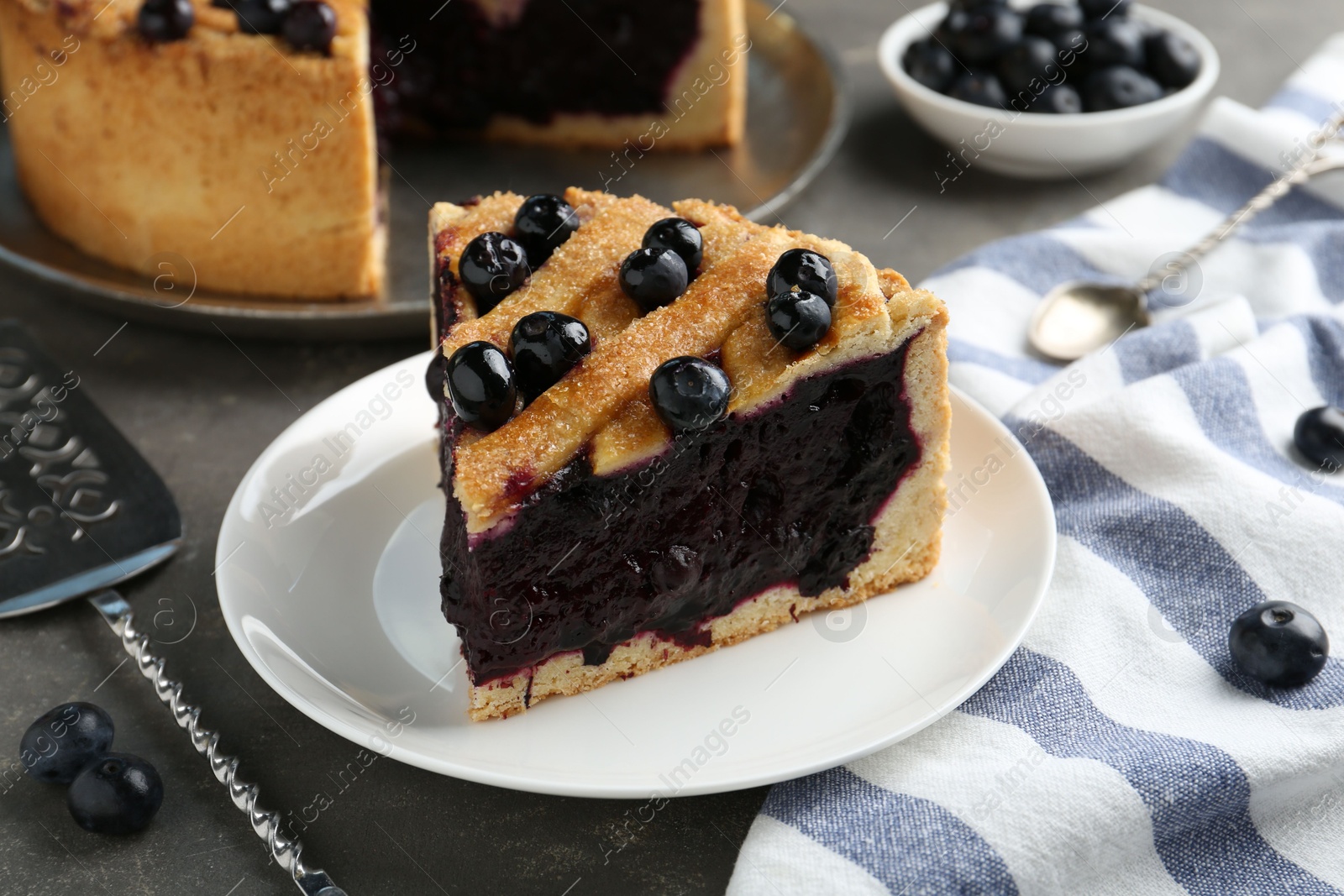 Photo of Slice of delicious homemade blueberry pie served on grey table, closeup