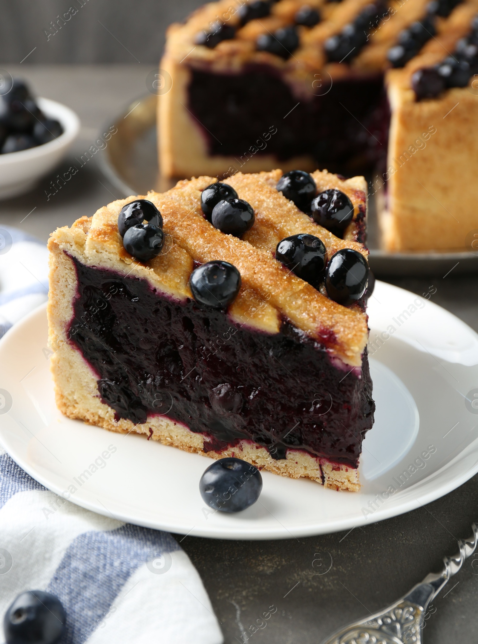 Photo of Slice of delicious homemade blueberry pie served on grey table, closeup