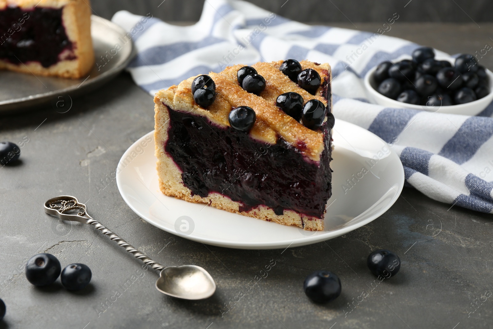 Photo of Slice of delicious homemade blueberry pie served on grey table, closeup