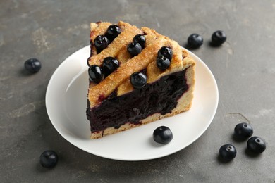 Photo of Slice of delicious homemade blueberry pie served on grey table, closeup