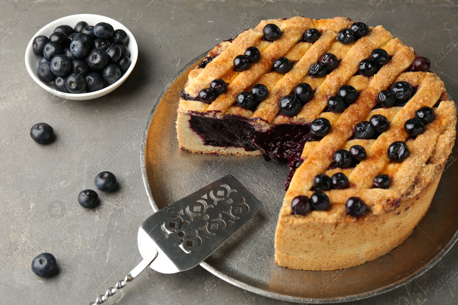 Photo of Cut homemade blueberry pie on grey table, closeup