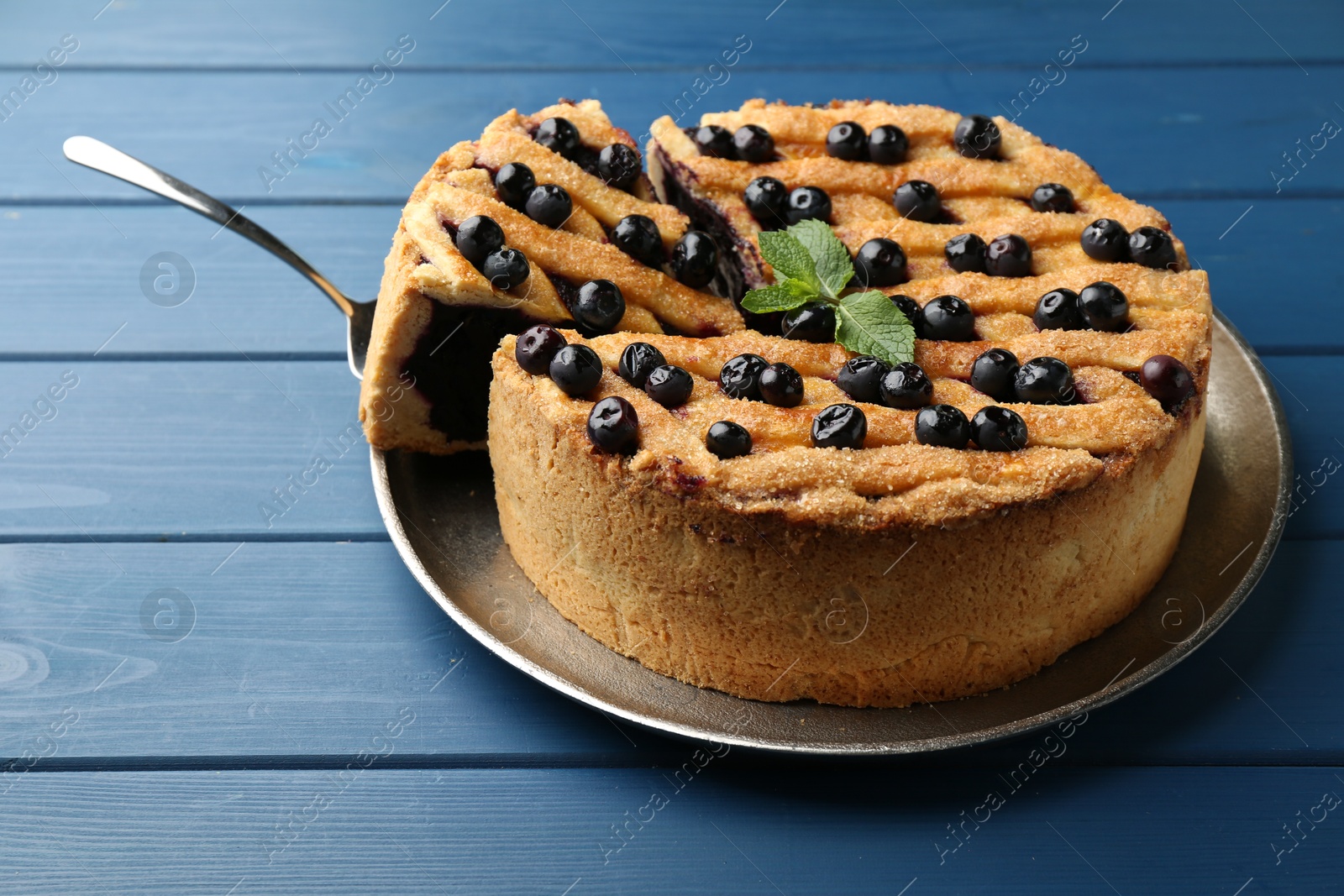 Photo of Taking slice of homemade blueberry pie on blue wooden table, closeup