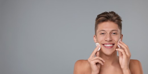 Handsome young man cleaning face with cotton pads on grey background. Banner design with space for text