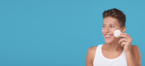 Handsome young man cleaning face with cotton pad on light blue background. Banner design with space for text