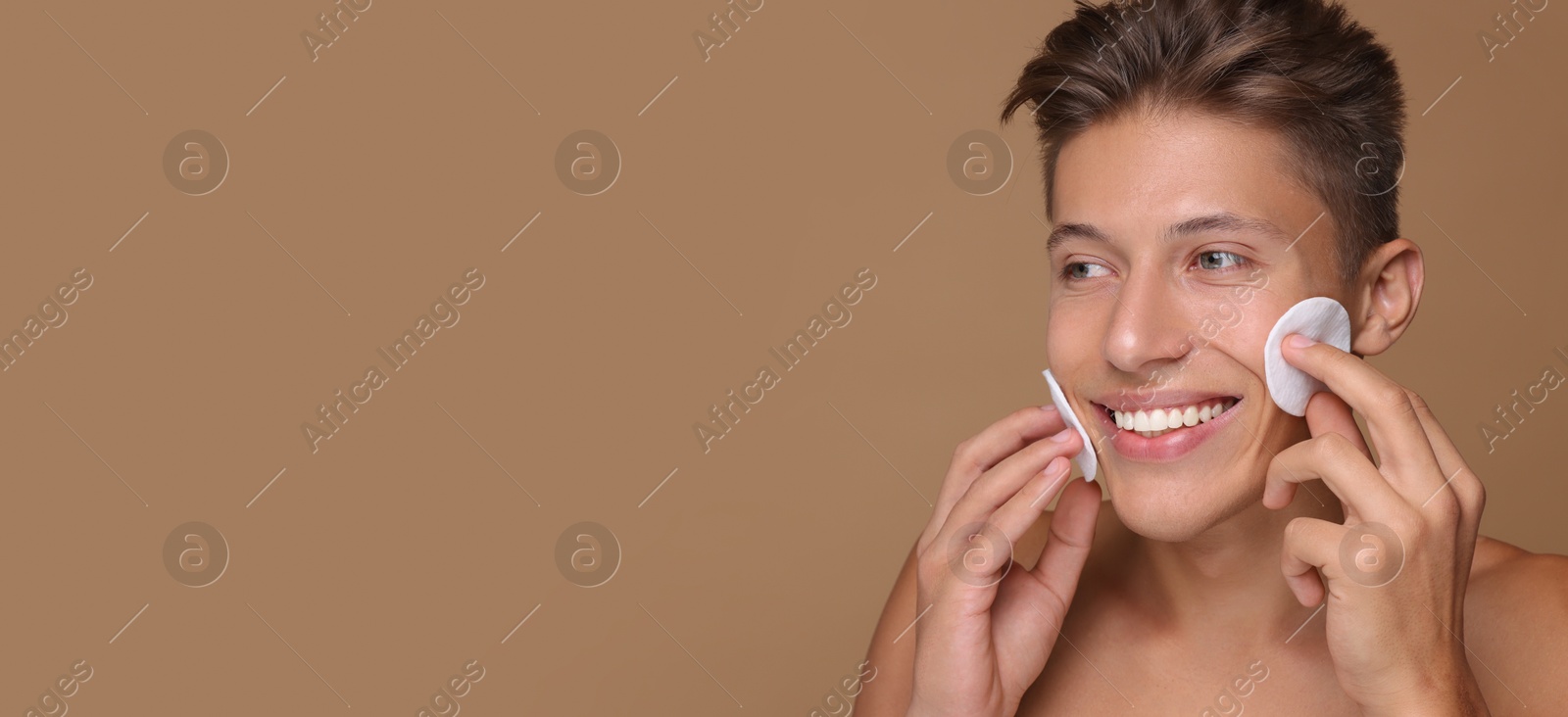 Image of Handsome young man cleaning face with cotton pads on dark beige background. Banner design with space for text