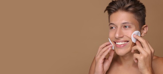 Image of Handsome young man cleaning face with cotton pads on dark beige background. Banner design with space for text