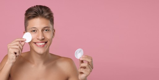 Handsome young man cleaning face with cotton pads on pink background. Banner design with space for text