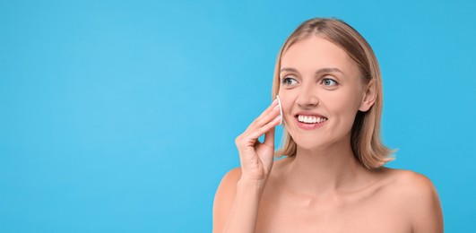 Image of Young woman cleaning face with cotton pad on light blue background. Banner design with space for text