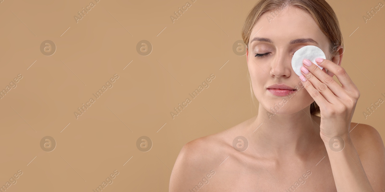 Image of Young woman cleaning her face with cotton pad on dark beige background. Banner design with space for text