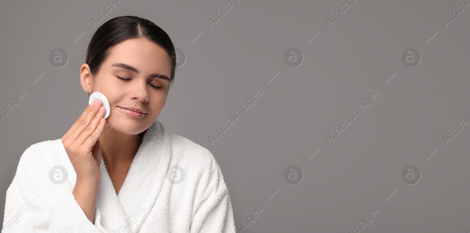 Image of Young woman cleaning her face with cotton pad on grey background. Banner design with space for text