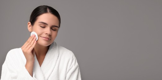 Image of Young woman cleaning her face with cotton pad on grey background. Banner design with space for text