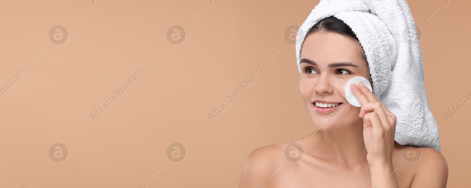 Image of Young woman cleaning her face with cotton pad on dark beige background. Banner design with space for text