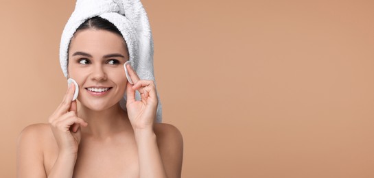 Young woman cleaning her face with cotton pads on dark beige background. Banner design with space for text