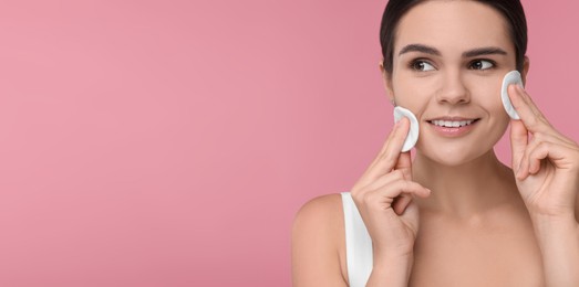 Image of Young woman cleaning her face with cotton pads on pink background. Banner design with space for text