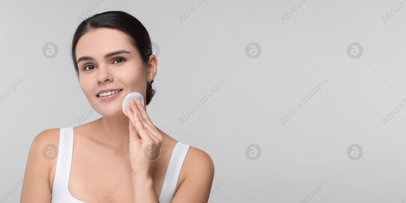 Image of Young woman cleaning her face with cotton pad on light grey background. Banner design with space for text