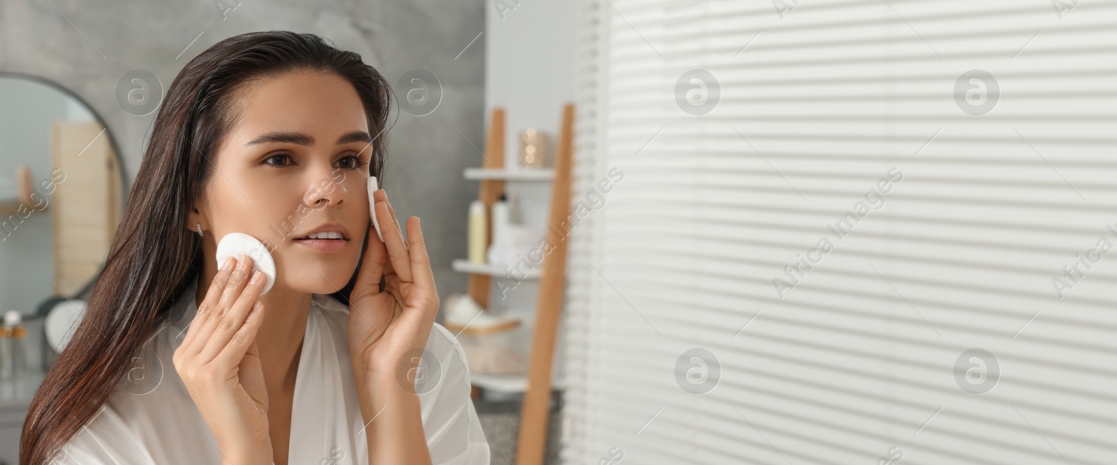 Image of Young woman cleaning her face with cotton pads in bathroom. Banner design with space for text