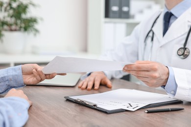 Photo of Doctor giving prescription to patient at wooden table in clinic, closeup