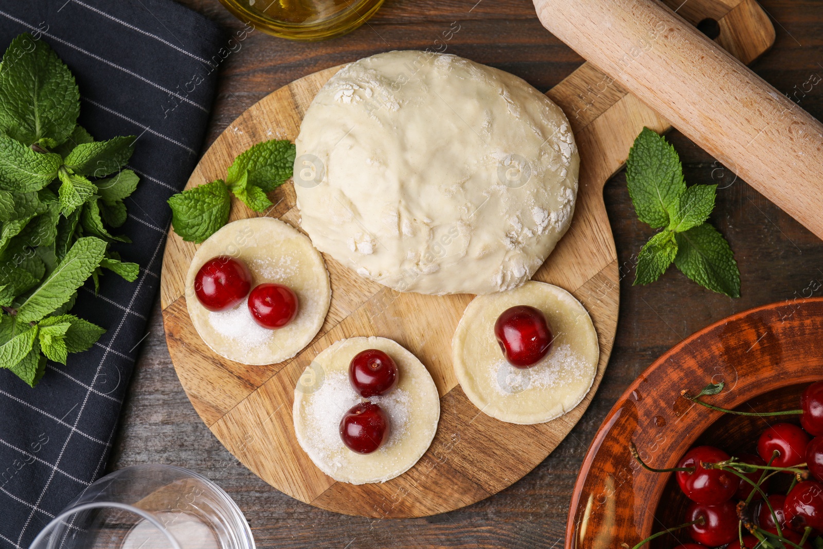 Photo of Process of making dumplings (varenyky) with cherries. Raw dough and ingredients on wooden table, flat lay