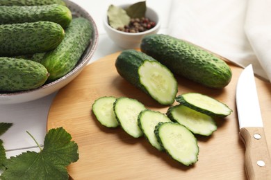 Photo of Fresh whole and cut cucumbers with knife on white table