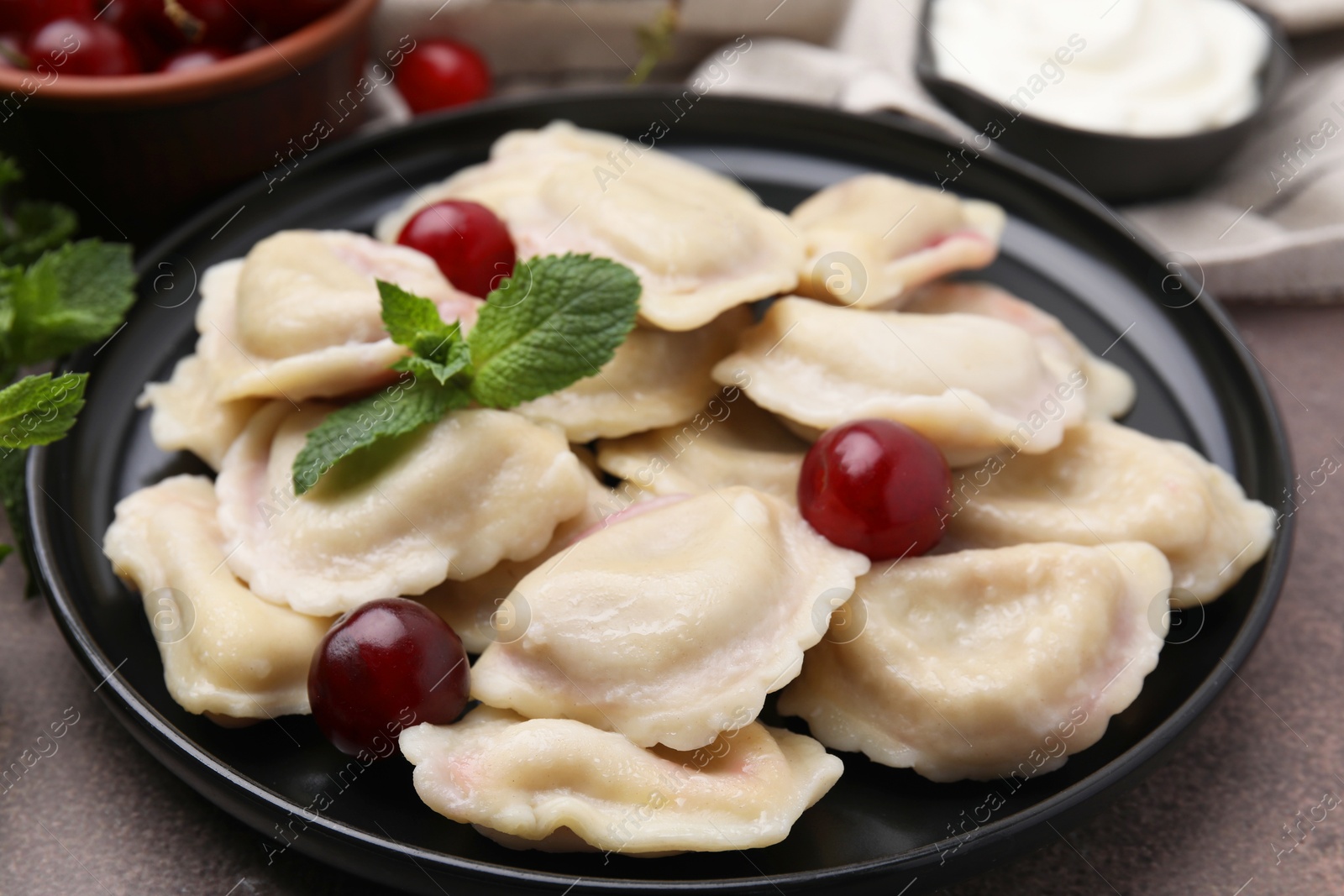 Photo of Traditional Ukrainian dumplings (varenyky) with cherries served on brown table, closeup