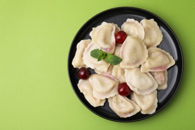 Photo of Traditional Ukrainian dumplings (varenyky) with cherries on green background, top view. Space for text