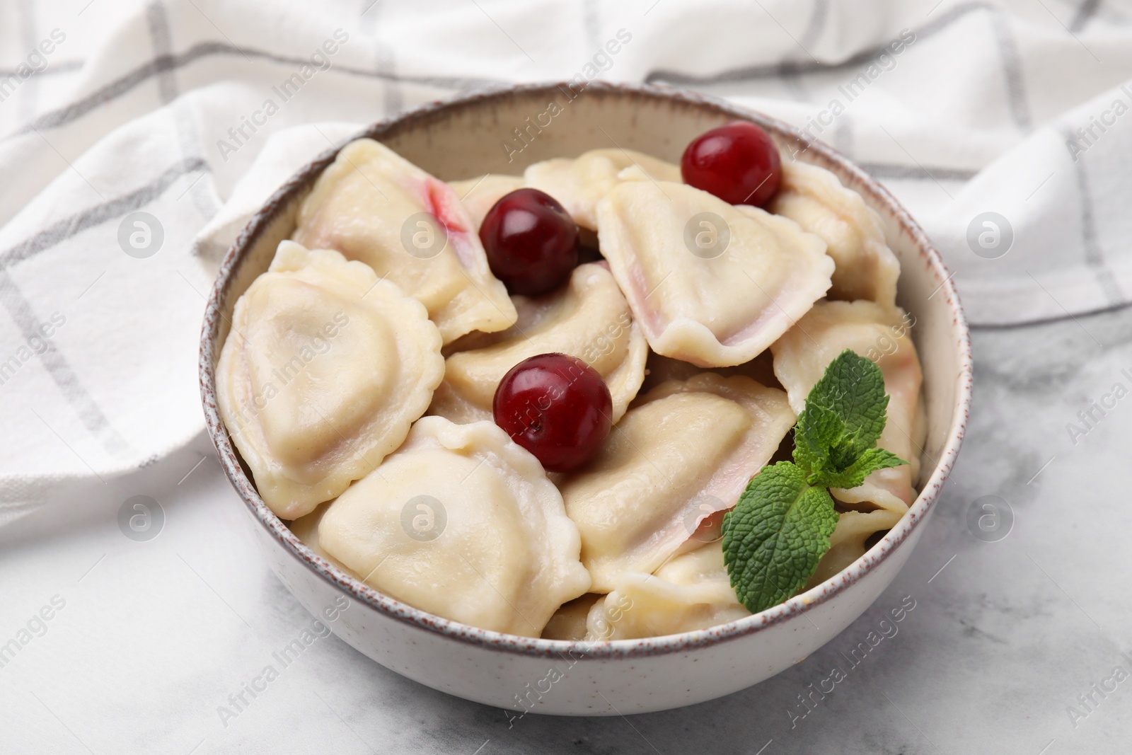 Photo of Traditional Ukrainian dumplings (varenyky) with cherries served on white marble table, closeup