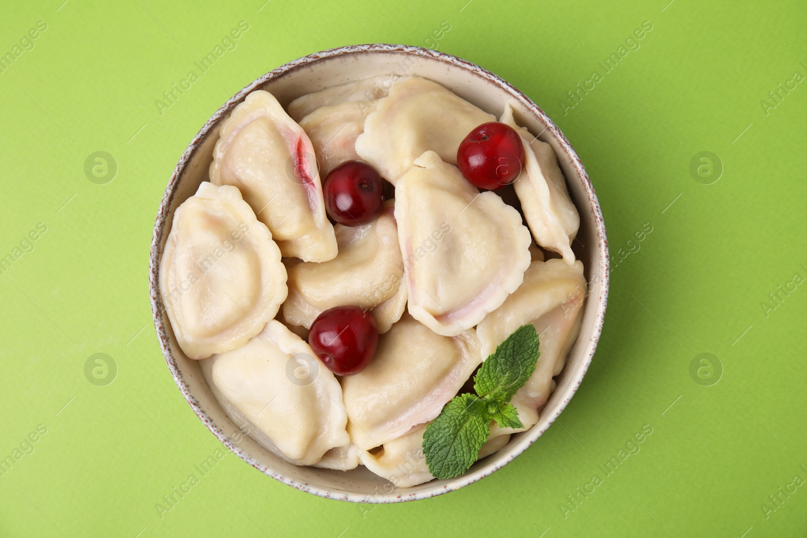 Photo of Traditional Ukrainian dumplings (varenyky) with cherries on green background, top view