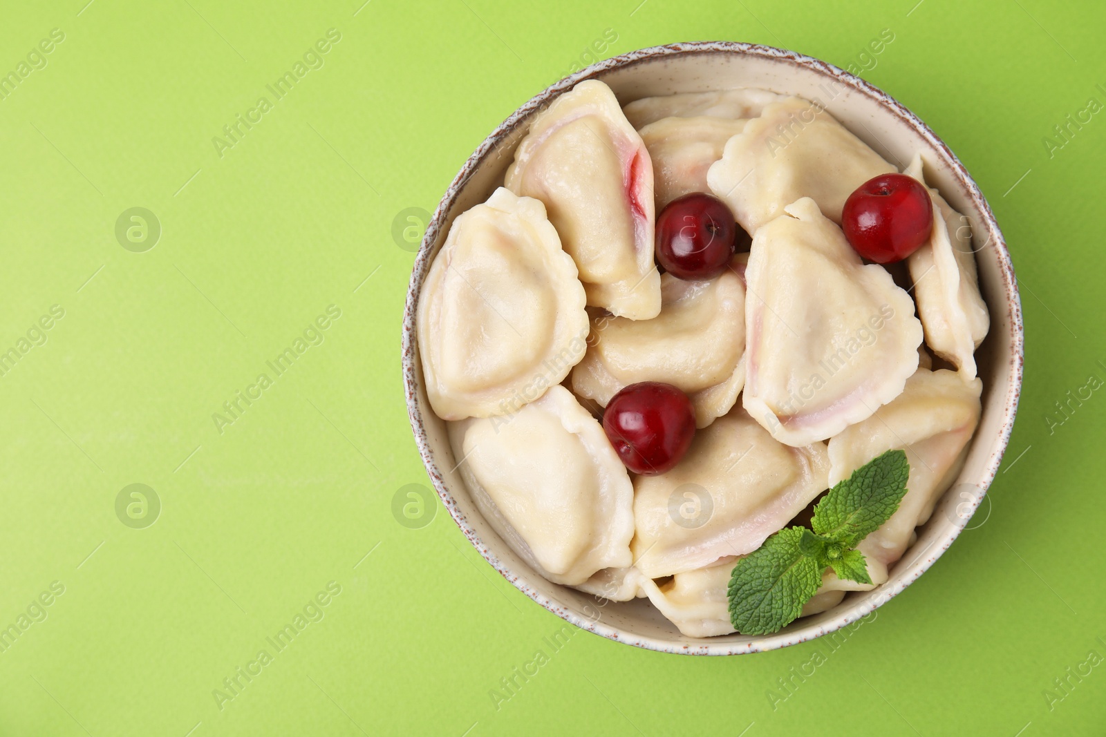 Photo of Traditional Ukrainian dumplings (varenyky) with cherries on green background, top view. Space for text