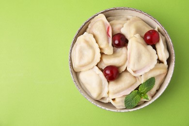 Traditional Ukrainian dumplings (varenyky) with cherries on green background, top view. Space for text