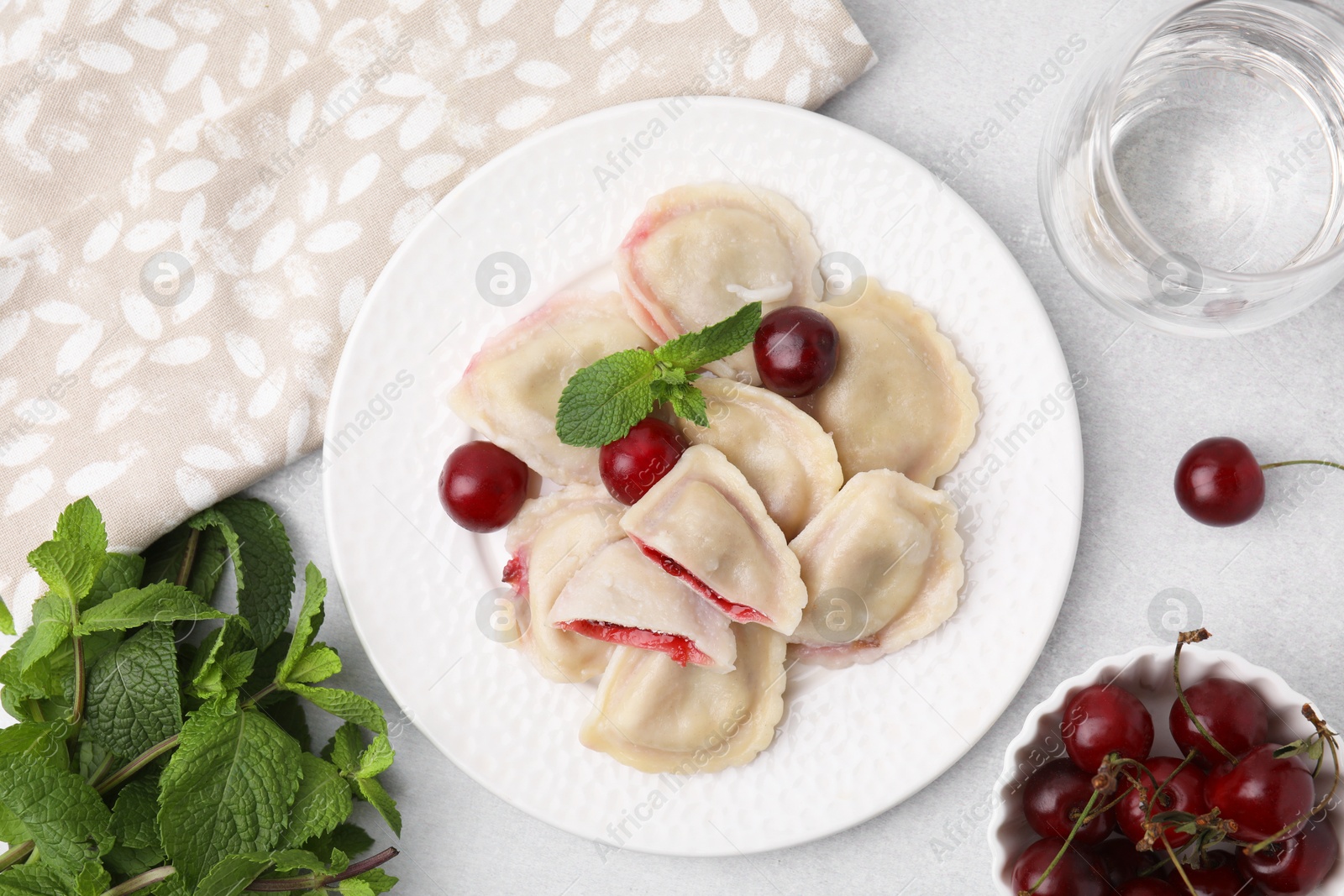 Photo of Traditional Ukrainian dumplings (varenyky) with cherries served on light table, flat lay