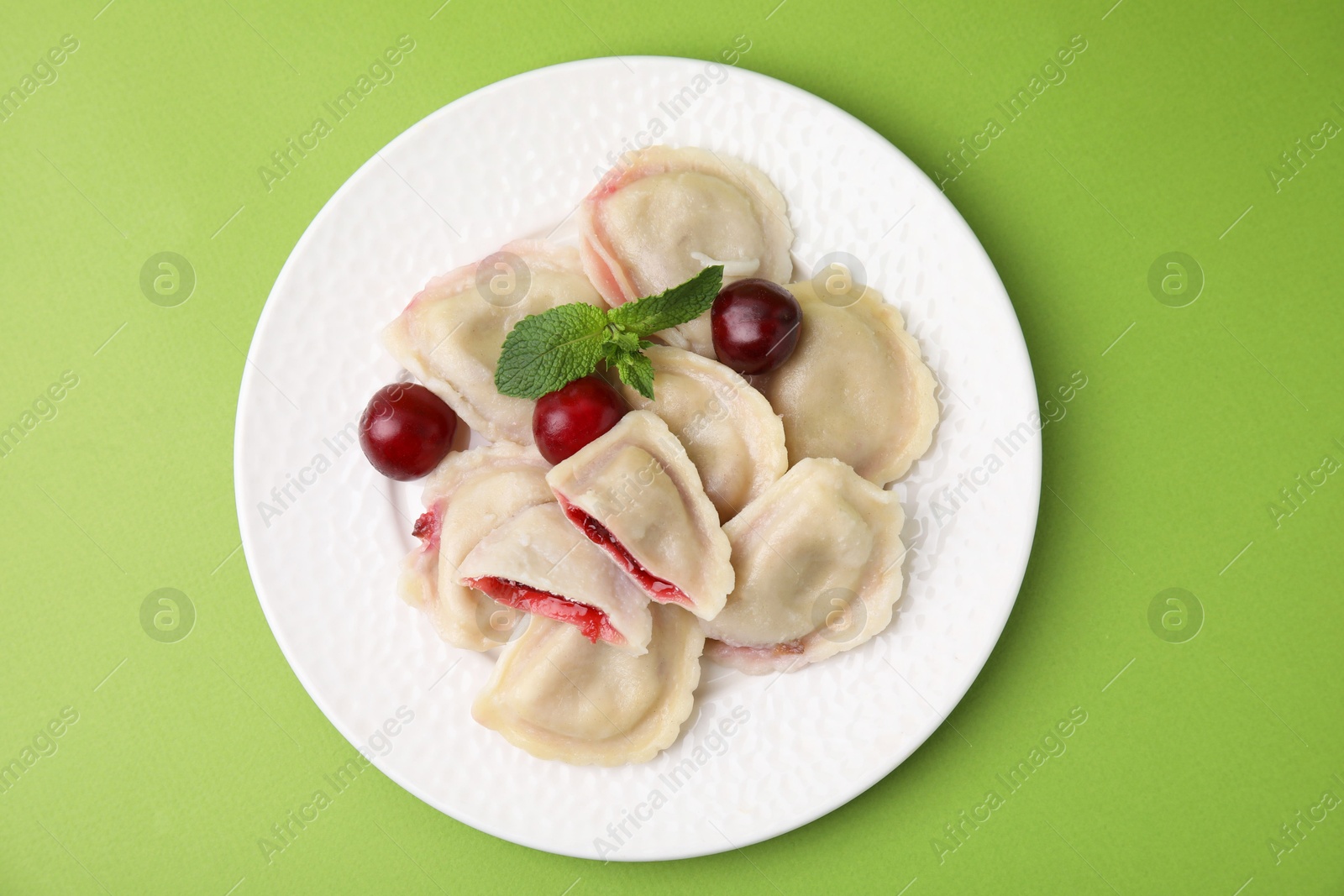 Photo of Traditional Ukrainian dumplings (varenyky) with cherries on green background, top view