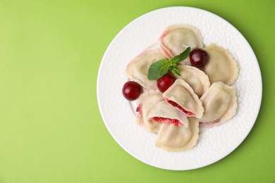 Photo of Traditional Ukrainian dumplings (varenyky) with cherries on green background, top view. Space for text