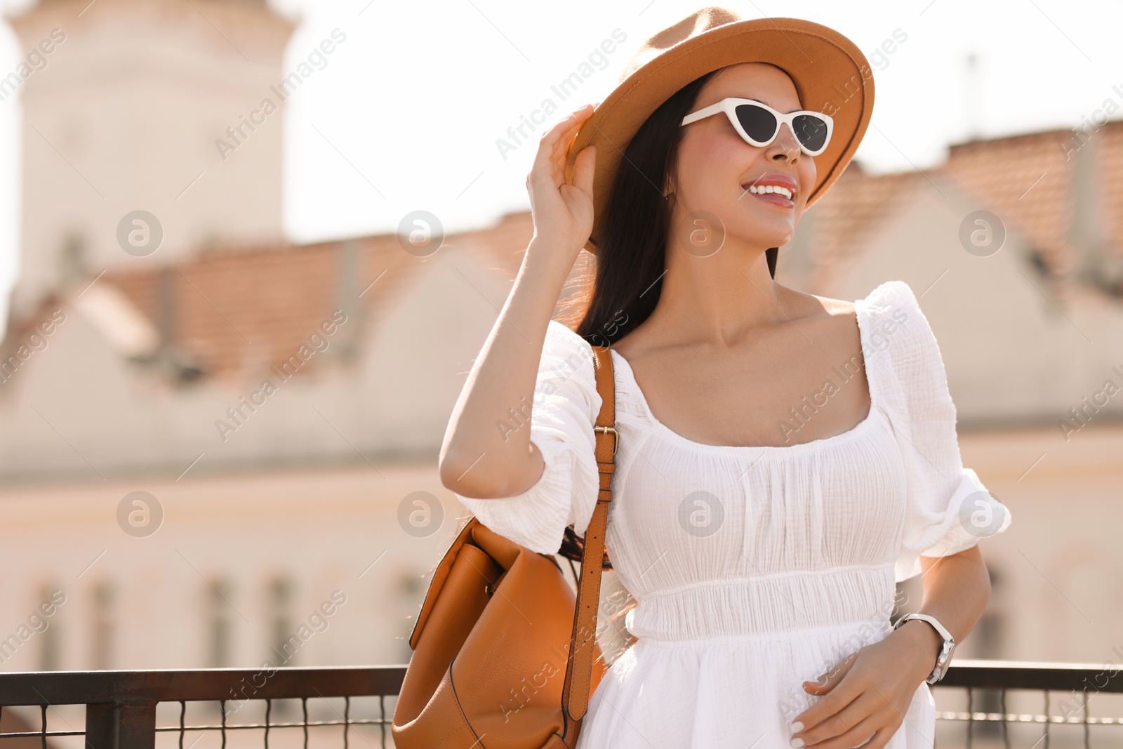 Photo of Smiling woman in stylish hat and sunglasses with backpack on city street