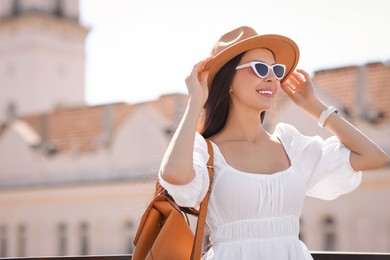 Smiling woman in stylish hat and sunglasses with backpack on city street