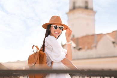 Smiling woman in stylish hat and sunglasses with backpack on city street