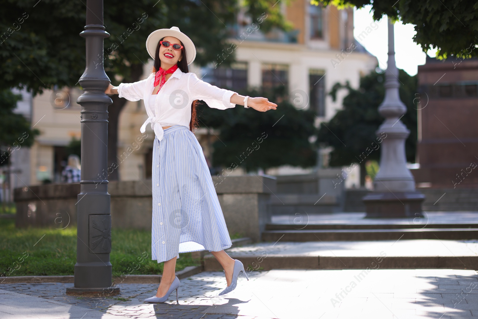 Photo of Smiling young woman in stylish hat and sunglasses on city street, space for text