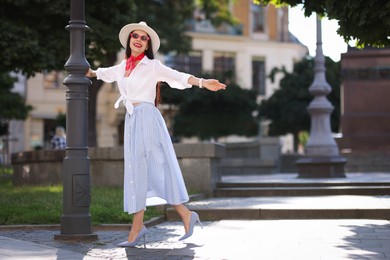 Smiling young woman in stylish hat and sunglasses on city street, space for text